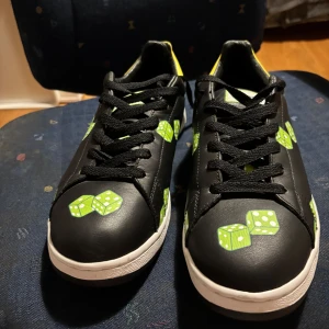 Ice Cream Footwear sneakers med tärningar - Unika svarta sneakers från Ice Cream Footwear med gröna tärningsmotiv och vit sula. Skorna har svarta skosnören och en gul detalj på hälen. Tillverkade i skinn och är en limiterad upplaga, numrerade 1273 av 2000. Ingen box eller kvitto medföljs