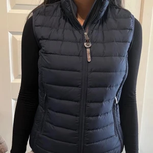 Parajumper väst  - Parajumper dunväst med quiltad design och hög krage. Västen har en hel dragkedja framtill och två sidofickor med dragkedja. Perfekt att slänga över en hoodie eller långärmad tröja för extra värme. Enkel och stilren look som funkar till det mesta.