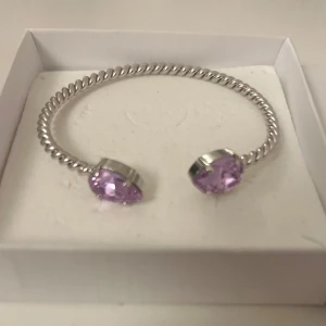 Silverfärgat armband Caroline Svedbom - Snyggt armband från Caroline Svedbom i silverfärgad metall med violetfärgade stenar i varje ände. Perfekt accessoar för att lyfta din outfit. Nypris: 795kr Mycket fint skick! 