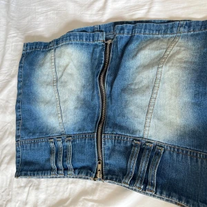 Blå jeanskjol med dragkedja - Säljer en blå jeanskjol med cool tvättad look och markerade sömmar. Kjolen har en synlig dragkedja framtill, fickor bak och snygga detaljer vid midjan. Perfekt för dig som gillar en avslappnad men trendig stil.