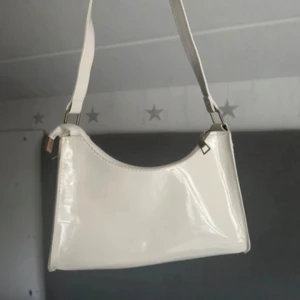 Vit axelväska i glansigt material - Snygg vit axelväska med stilren och enkel design. Väskan har en glansig finish och justerbart axelband. Perfekt storlek för det viktigaste och passar till många olika outfits.