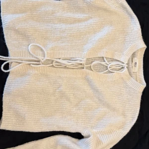 Vit kofta med snörning från Gina Tricot - Superfin vit kofta från Gina Tricot i ullblandning. Den har snygg snörning framtill och ribbade kanter vid ärmslut och nederkant. Perfekt att ha över ett linne eller ensam. 