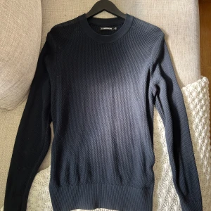 Svart stickad tröja från J.Lindeberg - Snygg marinblå stickad tröja från J.Lindeberg med rund halsringning och diskret struktur i materialet. Tröjan har långa ärmar och ribbade muddar vid ärmslut och nederkant. Skick: 10/10   Nypris: 1699kr  strl S