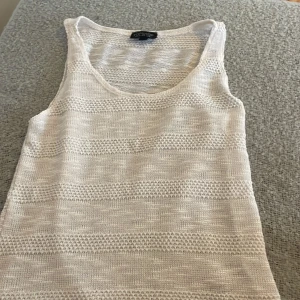 Vit stickad linnetopp från Topshop - Säljer en vit stickad linnetopp från Topshop i storlek 36. Toppen har ett snyggt mönster med genombrutna ränder och är ärmlös med rund halsringning. Perfekt för varma dagar och enkel att styla till olika outfits.💕