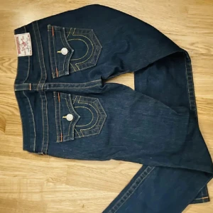 Mörkblå bootcut jeans från True Religion - Säljer ett par mörkblå jeans från True Religion med bootcut passform ”24”. Jeansen har dekorativa fickor bak med vita sömmar och silverfärgade knappar. Klassisk femficksmodell och låg midja. Säljer för de inte passade mig, men supersnygga och jättebra pris  