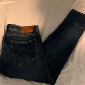 Replay jeans  - Säljer ett par snygga Replay jeans i mörkblå med klassiskdesign och knäppning fram. Jeansen har raka ben och diskreta slitningar för en cool look. Perfekta för dig som gillar stilrena och tidlösa jeans.