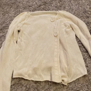 Vit stickad kofta med knappar - Säljer en vit stickad kofta med två knappar framtill och lång ärm. Koftan har en asymmetrisk nederkant och är mjuk i materialet. 💖