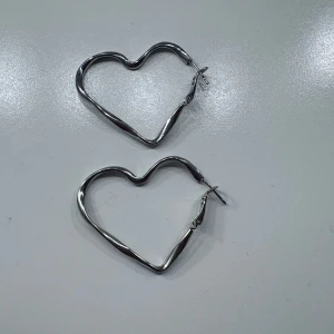 Hjärtformade örhängen i silverfärg - Säljer ett par stora örhängen i form av hjärtan. De är i silverfärgad metall och har en enkel låsmekanism. Perfekta för att ge din look en söt och trendig touch.