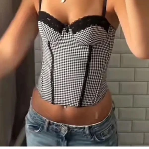 Svartvit rutig korsettopp från hm  - Säljer en snygg korsettopp i svartvitt rutigt mönster med svarta spetsdetaljer upptill. Toppen har smala axelband och markerade sömmar framtill för en trendig look. Perfekt att styla med jeans eller kjol. Storlek M💗