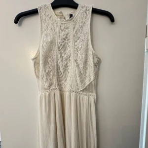Vit spetsklänning med plisserad kjol - Säljer en  vit klänning med spets upptill och plisserad kjol. Klänningen är lite beige vit. Perfekt för sommarens speciella tillfällen 🩷