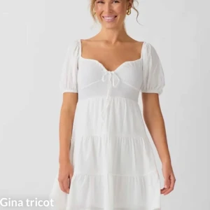 Klänning från Gina Tricot - Supersöt vit klänning från Gina Tricot med puffärmar och knytning framtill. Klänningen har en luftig passform, volangdetaljer och är tillverkad i ett lätt, strukturerat material. 