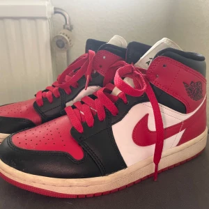 Nike Air Jordans i rött, svart och vitt - Säljer ett par klassiska Nike Air Jordans med högt skaft. Skorna har en snygg färgkombination av rött, svart och vitt med röda skosnören och ikonisk Air Jordan-logga på sidan. Perfekta för dig som gillar streetwear och sneakers med attityd.