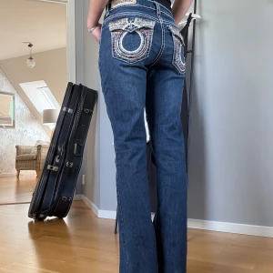 Blå jeans från Denim Couture med broderade fickor - Säljer ett par blå jeansbyxor från Denim Couture med unika broderade bakfickor. Byxorna är bootcut med tydliga kontrastsömmar. Jag är 164, står ingen storlek men skulle säga 25/32. Midjemått:  81cm Innerben: 82,5cm. Bild 4: en tråd är lös men syns ej när fickan är ”stängd”