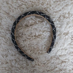 Svart och vit diadem med rutigt mönster - Snyggt diadem i svart och vitt med rutigt mönster. Perfekt accessoar för att lyfta din look. Diademet har en vadderad form och är klätt i tyg. Kände att den inte passade min stil så säljer den nu!
