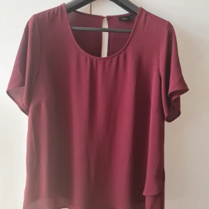 Blus från Zizzi strl 48 (M) - Säljer en elegant vinröd blus från Zizzi. Blusen har korta ärmar och en rund halsringning. Den är tillverkad i ett lätt och luftigt material, perfekt för både vardag och fest. Baksidan har en liten knappdetalj vid nacken. Storlek M (48). Kan hämtas i Vallentuna.