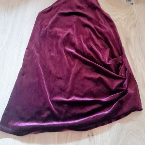 Vinröd ärmlös festtopp från Gina Tricot - Vinröd ärmlös topp i mjukt sammets liknande material från Gina Tricot. Den har en snygg öppning i ryggen och är tillverkad i stretchigt material för en bekväm passform. Perfekt för dig som vill sticka ut med en elegant look. Använd en gång 