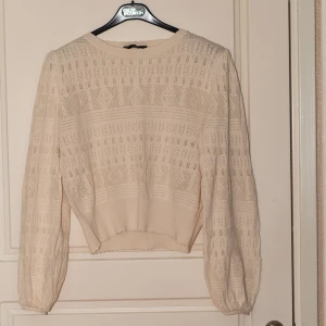 Beige stickad tröja med spetsmönster - Säljer en beige stickad tröja med vackert spetsmönster och lång ärm. Tröjan har rund halsringning och är lätt croppad i modellen. Perfekt för lager-på-lager under höst och vår.