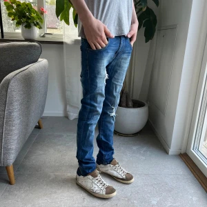 Levi's 519 Skinny Jeans i blå denim - Säljer ett par Levi's 519 skinny jeans i klassisk blå denim med slitningar på benen. Byxorna har fem fickor, dragkedja och knapp, samt tydliga Levi's-detaljer som röd etikett och läderpatch bak. Perfekta för dig som gillar en smal passform och streetstil.