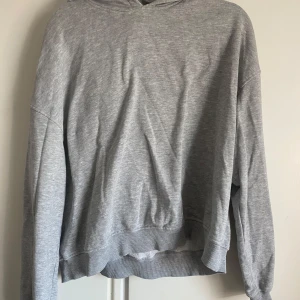 Grå hoodie - En klassisk grå hoodie med huva och långa ärmar. Tröjan har ribbade muddar vid ärmslut och nederkant. Perfekt för en avslappnad stil och enkel att matcha med det mesta.