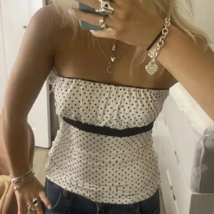 Vit prickig tubtopp med volang - SÖKER!! I storlek S 💘💘En söt vit tubtopp med svarta prickar och volang upptill. Toppen har en svart kant under bysten som ger en fin kontrast. 