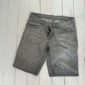 Grå jeansshorts med dragkedja - Snygga grå jeansshorts med klassisk femficksdesign, dragkedja och knapp framtill. Perfekta för en avslappnad stil under varmare dagar. Passar dig som gillar en enkel och stilren look.