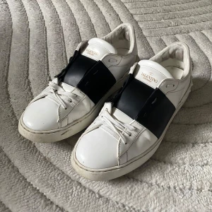 Valentino Open - Säljer ett par snygga Valentino Garavani Open sneakers i vitt skinn med svart detalj över mitten. Klassisk rund tå, platt sula och vita skosnören. Kommer med originalförpackning och dustbags.