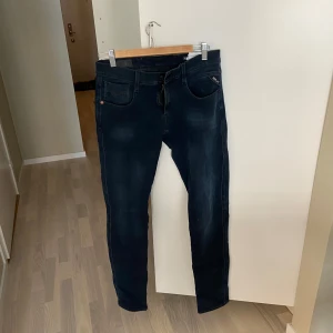 Mörkblå jeansbyxor från Replay Anbass - Säljer ett par mörkblå jeans från Replay med klassisk femficksdesign och svarta detaljer. Jeansen har en smal passform och är perfekta för dig som gillar en stilren look. Snygga att matcha med både t-shirt och skjorta.