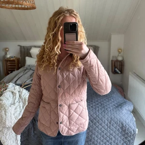 Rosa quiltad jacka från Barbour - Säljer en ljusrosa quiltad jacka från Barbour med tryckknappar och två stora fickor framtill. Orginalpris runt 3000kr, behandlats med försiktighet. 