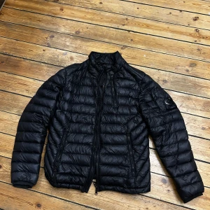  CP Company D.D Shell Down Jacket - Svart L - Köpt på Harrods i London - en svart dunjacka från CP Company med dragkedjor. Jackan har en CP Company-logga på ärmen. Perfekt för vår och höst dagar och enkel att matcha med olika outfits. CP Company används ofta av de som även gillar Stone Island.