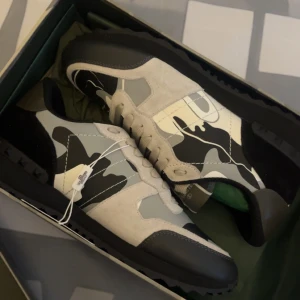 sneakers med camo-mönster - Rockrunner sneakers med svart, vit och grå camouflage. Skorna har svarta gummisulor, rund tå och klassisk snörning. Ikonisk design med blandade material och detaljerad finish.
