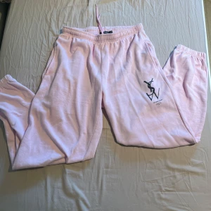 Ljusrosa mjukisbyxor från Boohoo - Ljusrosa mjukisbyxor från Boohoo med resår i midjan och snörning. Byxorna har sidofickor och tryckt logga på ena sidan