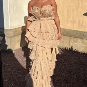 Beige axelbandslös långklänning med volanger - Säljer en beige axelbandslös långklänning med flera lager volanger och asymmetrisk nederkant.  Dem två första bilderna är på en tjej som är 155cm, resten är på en tjej som är 170cm 🩷 Nypris 1849kr, klänningen är i väldigt bra skick! 