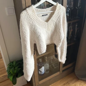 stickad croppad tröja från Gina Tricot - Mysig vit stickad tröja från Gina Tricot med croppad passform och bred v-ringning. Tröjan har långa ärmar och är perfekt för lager-på-lager-stil. Snygg och enkel att matcha till olika outfits.