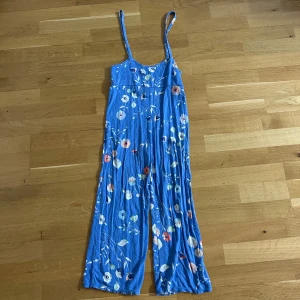 Blå blommig hängselbyxor med smala axelband - Säljer blåa hängselbyxor med smala axelband och blommigt mönster. Byxorna har en avslappnad passform och är perfekt för varma dagar. Perfekt att styla med en T-shirt eller topp! Står ingen storlek men skulle gissa på XXS/XS. Köpt utomlands! Går över anklarna på mig som är 163 cm! 
