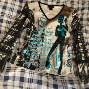 Cool tröja  - Tröja med tre kvarts ärmar som är i bra skick. Är v-ringad. Har coolt print, svartvita ärmar och på framsidan är den en kvinna och text i blå. Det står att det är 100% cotton. Skulle säga att det är storlek S - M