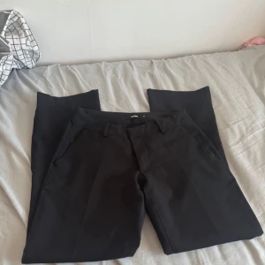 lågmidjade kostymbyxor  - Snygga svarta kostymbyxor från Bik Bok med klassisk rak passform och hällor för bälte. Byxorna har fickor fram och dekorfickor bak, perfekta till en stilren look.