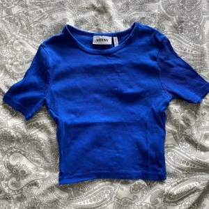 Blå ribbad croppad topp från Weekday - Säljer en blå ribbad croppad topp från Weekday. T-shirten har korta ärmar och rund halsringning. Perfekt att matcha med jeans eller kjol för en snygg look.
