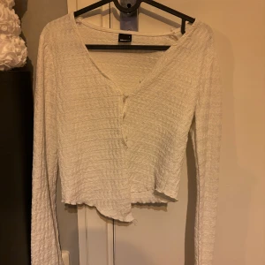 Vit croppad kofta med knappar - Säljer en vit croppad kofta från Bik Bok med v-ringning och knappar framtill. Tröjan har lång ärm och är tillverkad i ett ribbat, mjukt material. Perfekt att styla med jeans eller kjol.
