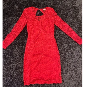 Röd spetsklänning från Vero Moda - Säljer en röd, figurnära spetsklänning från Vero Moda med lång ärm och vackert blommönster. Klänningen har en snygg öppen detalj i ryggen och är kort i modellen. Storlek S, passar nog även M. 