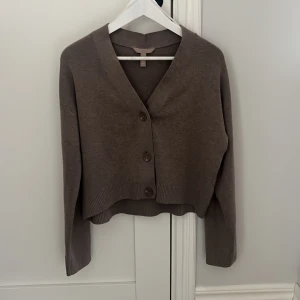 Brun  kofta från H&M - Mysig brun kofta från H&M med stora knappar framtill. Tröjan har långa ärmar och bred ribbad kant vid ärmslut och vid magen.