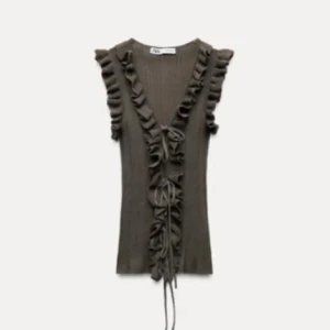 Svart volangtopp med knytning - Säljer denna slutspels Zara toppen med volangdetaljer längs v-ringningen och axlarna. Toppen har knytning framtill och är figurnära i passformen!❤️