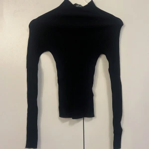 Svart ribbad polotröja - Säljer en svart ribbad polotröja med lång ärm. Tröjan är tight i modellen och har en hög polokrage. Perfekt att styla med jeans eller kjol för en stilren look. Storlek S från New Yorker.