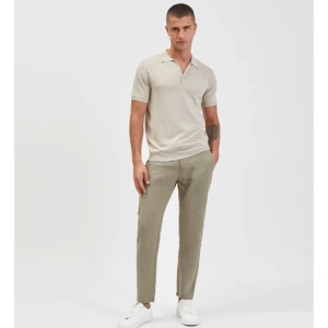 Beige pikétröja med krage - Säljer en stilren beige pikétröja med klassisk krage och korta ärmar. Tröjan har knappar framtill och är tillverkad i ett mjukt material som känns skönt mot huden. Perfekt för en clean och avslappnad look.