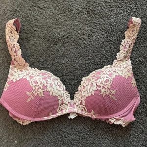 Rosa spets-bh med blommönster - Säljer en romantisk rosa bh med vacker beige spets och blommönster. Bh:n har vadderade kupor och breda axelband dekorerade med spets. Perfekt för dig som vill ha något både sött och elegant.