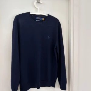 Mörkblå stickad tröja från Polo Ralph Lauren - Säljer en stilren mörkblå tröja från Polo Ralph Lauren i slim fit-modell. Tröjan har rund halsringning, långa ärmar och en diskret broderad logga på bröstet. Perfekt för dig som gillar klassisk och enkel stil.