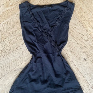 Svart ärmlös topp med spets från Vero Moda - Säljer en såå snygg svart ärmlös topp från Vero Moda med v-ringning och fina spetsdetaljer längs halsringningen. Toppen har en figurnära passform och är perfekt för dig som gillar stilrena plagg med en touch av spets.❤️