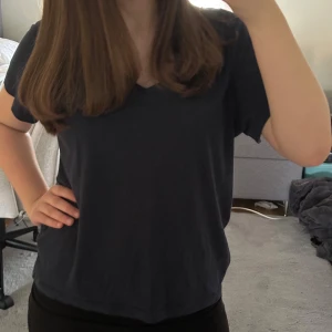 Mörkblå t-shirt med v-ringning - En basic mörkblå t-shirt med v-ringad hals. T-shirten har korta ärmar och en avslappnad passform. Perfekt till jeans eller shorts för en enkel och stilren look.