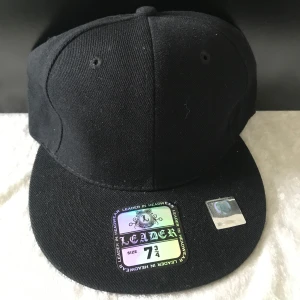 Svart keps från Leader - Säljer en klassisk svart keps från Leader med rak skärm och ventilation på ovansidan. Kepsen har en enkel och stilren design utan logga framtill. Perfekt för dig som gillar en clean look.