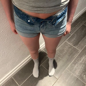 Blå jeansshorts från H&M - Säljer ett par klassiska blå jeansshorts från H&M med upprullade benslut och femficksdesign. De har normal passform och stängs med dragkedja och knapp. Perfekta för varma dagar och enkla att matcha med olika toppar. Hör av er vid frågor eller fler bilder.💛