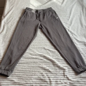 Grå mjukisbyxor från JJREBEL - Säljer ett par grå mjukisbyxor från JJREBEL med resår i midjan och benslut, samt snörning i midjan. Byxorna har sidofickor och en bakficka, perfekt för en avslappnad stil.